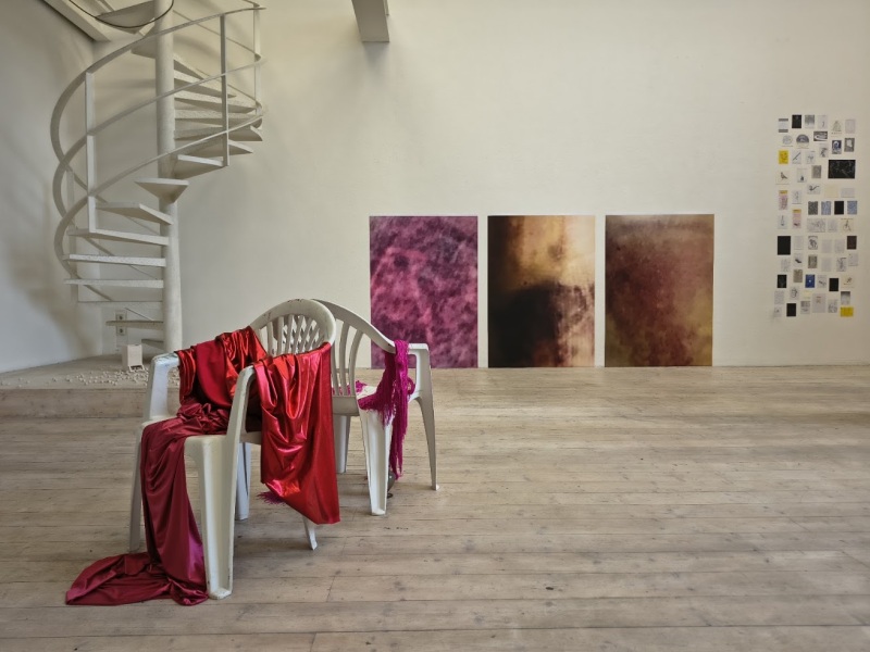 Plastiksessel mit übergeworfenen Stoffen im Vordergrund, Bilder an der Wand im Hintergrund